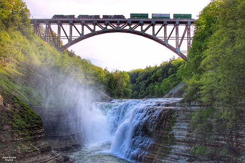 Beautiful red steel arch bridge spanning a waterfall, with a train crossing the bridge